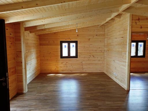 Interior de una habitación de madera, con ventanas y techo a dos aguas. Suelo de madera.