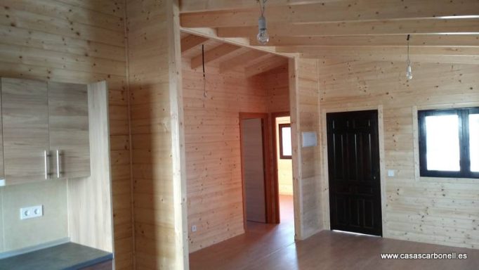 Interior de una casa con paredes de madera, ventanas y suelo de madera.