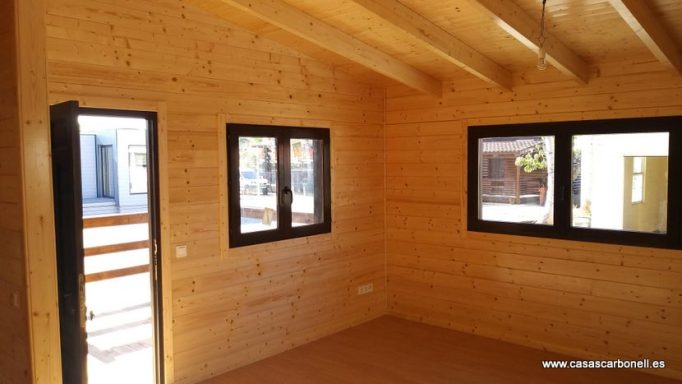 Interior de una habitación de madera con ventanas y puerta de acceso exterior.