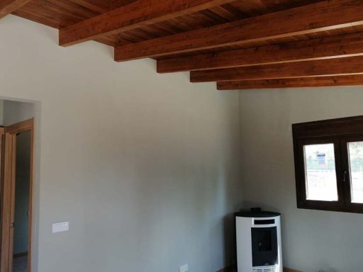 Interior de una habitación con techo de vigas de madera y estufa junto a una ventana.