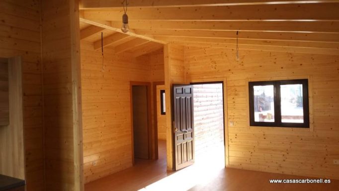 Interior de una casa de madera con paredes claras y puertas y ventanas oscuras.