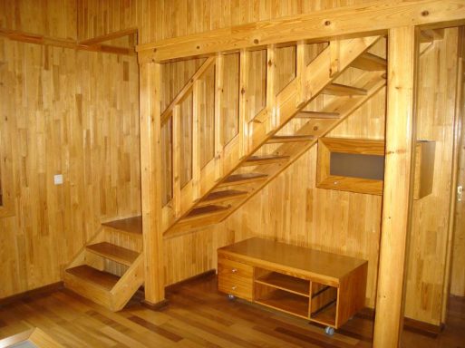 Escalera de madera en una habitación con paredes y suelo de madera. Mueble bajo junto a la pared.