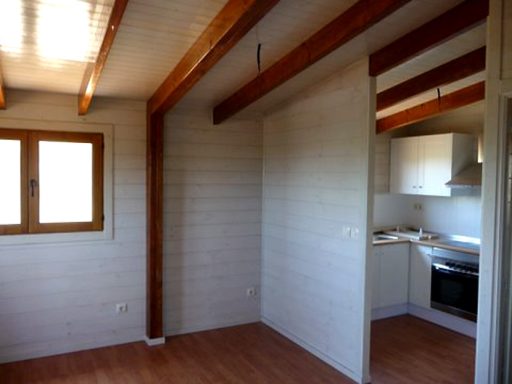 Interior de una habitación con techo de madera y cocina abierta. Paredes claras.