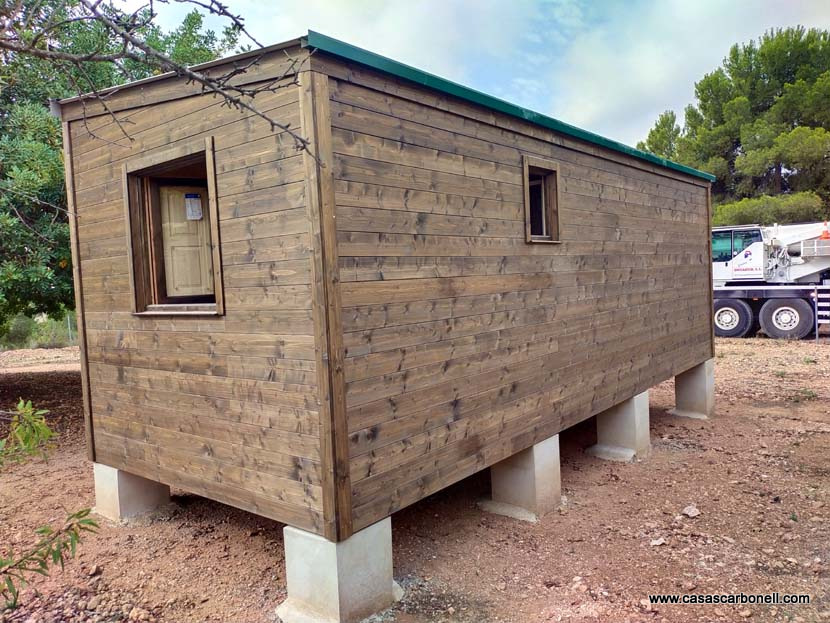 Pequeña construcción de casa de madera sobre pilotes, con ventanas y techo a dos aguas.