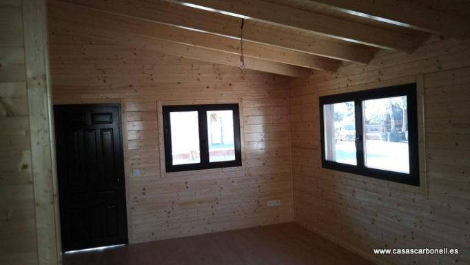 Interior de una habitación con paredes de madera, ventanas oscuras y puerta negra.