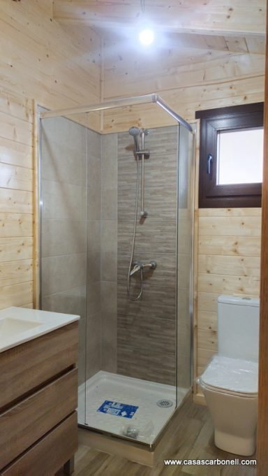 Baño moderno con ducha de cristal, lavabo y inodoro en un ambiente de madera clara.