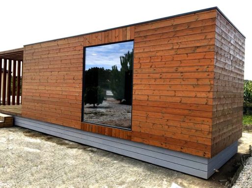 Casa prefabricada moderna de madera con un gran ventanal reflectante y base de metal.