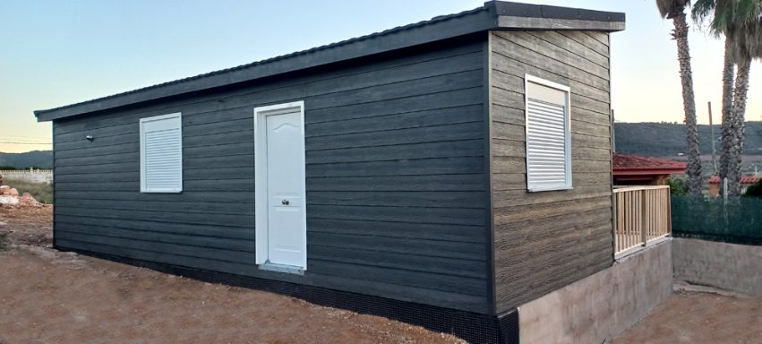 Casa prefabricada de madera de un solo piso, pintada de negro, con ventanas y puerta blanca.