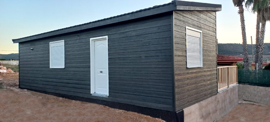 Casa prefabricada de color negro, con ventanas y puerta blanca, en un entorno natural.