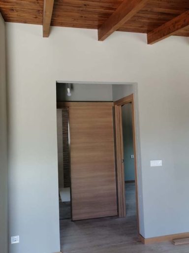 Puerta de madera en un interior moderno con paredes grises y techo de vigas.