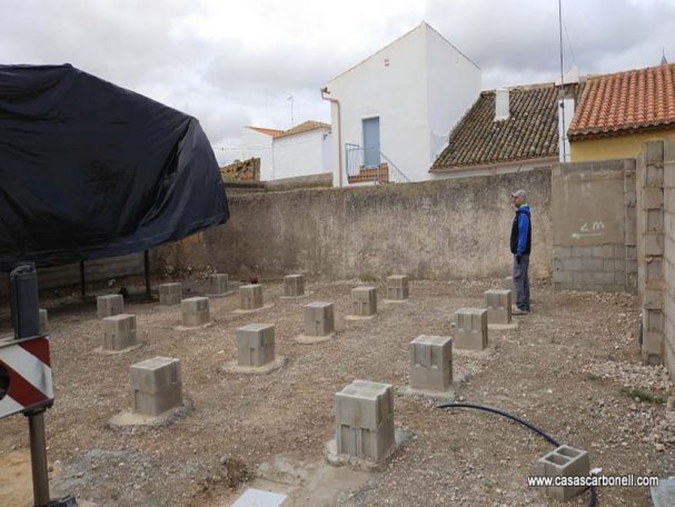 Base para casa prefabricada compuesta de pilares de bloques de hormigón Terreno vacío con pilares de concreto y una manguera, rodeado de muros.