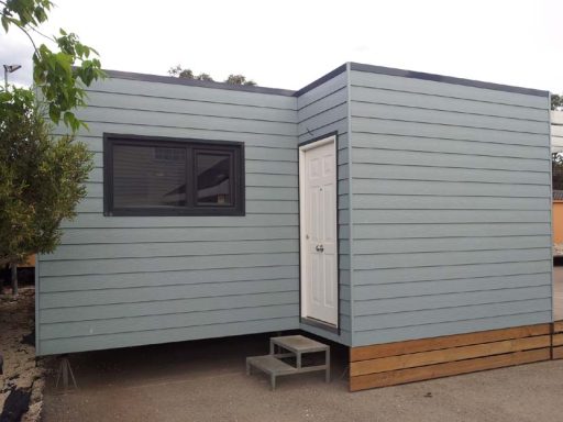 Casa prefabricada moderna de color azul con una puerta blanca y una ventana en la fachada.