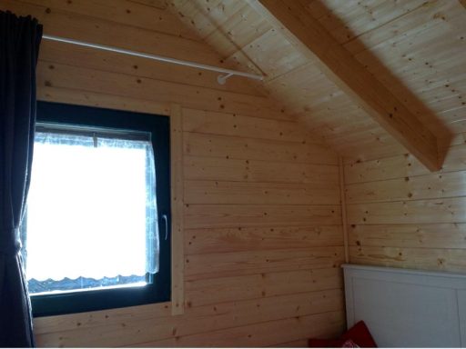 Interior de una habitación con paredes de madera y una ventana con cortina.