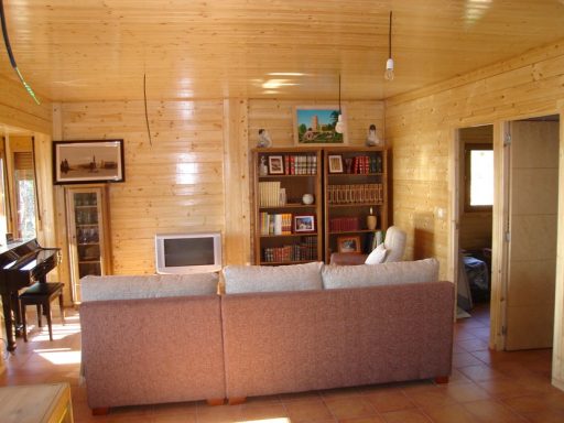 Interior de una cabaña de madera con sala de estar, estantería y piano.