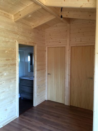 Interior de una cabaña de madera con paredes claras y dos puertas en las esquinas.