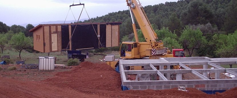 Montaje de una casa modular con grúa y estructura metálica en un terreno rural.