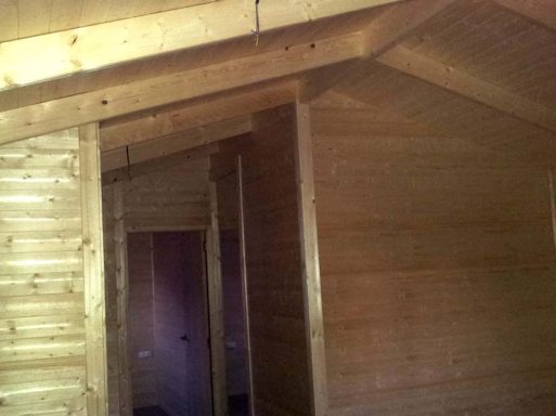 Interior de una cabaña de madera con paredes y techo de madera sin terminar.