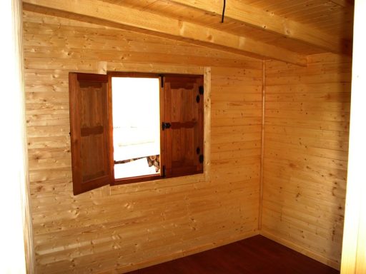 Interior de una habitación de madera con una ventana con contraventanas abiertas.