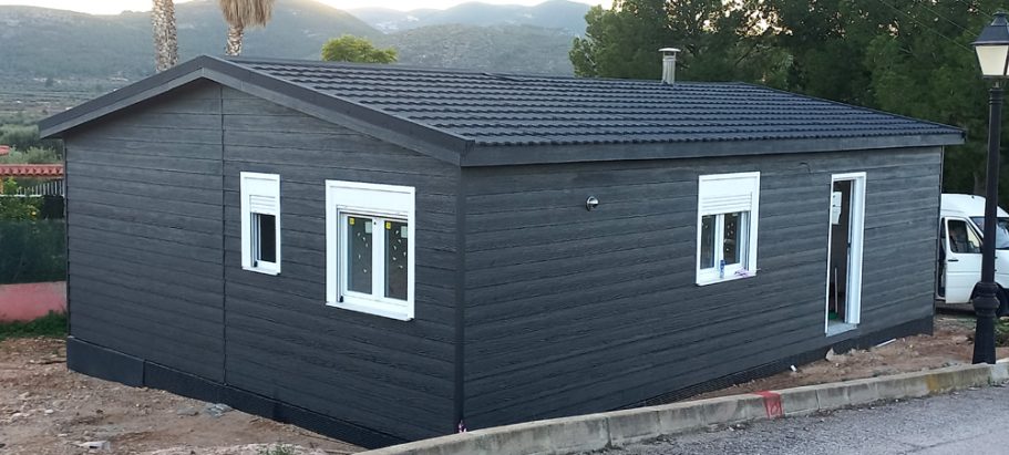 Casa prefabricada de color gris oscuro con ventanas y puerta blanca en un entorno natural.
