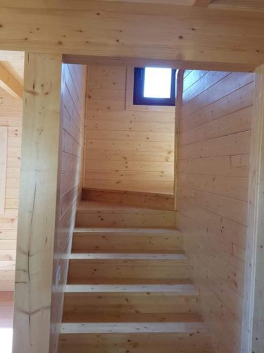 Escalera de madera en un interior con paredes de paneles de madera y una ventana pequeña.