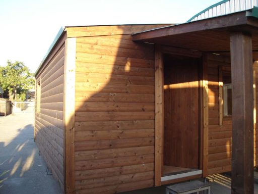 Cabin de madera con entrada, iluminada por el sol, situada en un entorno exterior.