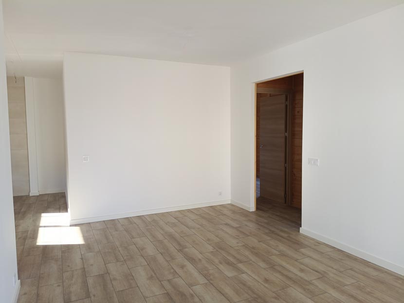 Habitación vacía con paredes blancas y suelo de madera clara, iluminada por la luz natural.