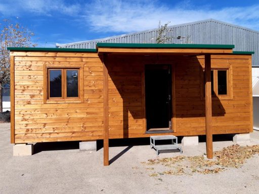 Casa de madera con una entrada, ventanas y escalones, en un entorno exterior.