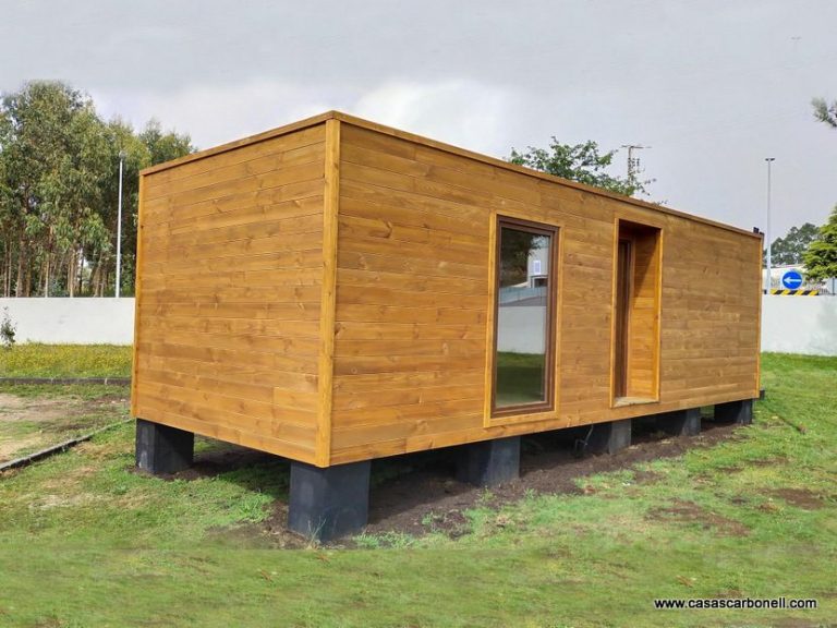 Casas prefabricadas de contenedor, casa de madera con ventanas, elevada sobre pilotes y ubicada en un terreno verde.