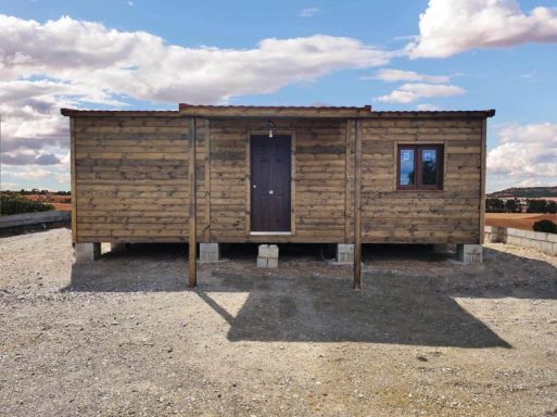 Casa de madera sobre pilotes, con puerta y ventana, en un paisaje despejado.