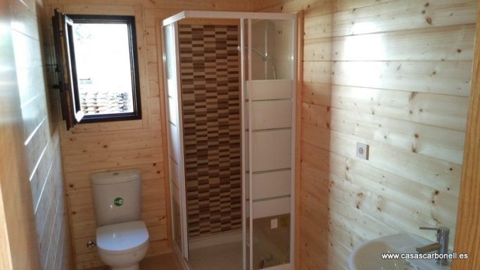 Baño de madera con ducha, inodoro y ventana al exterior.