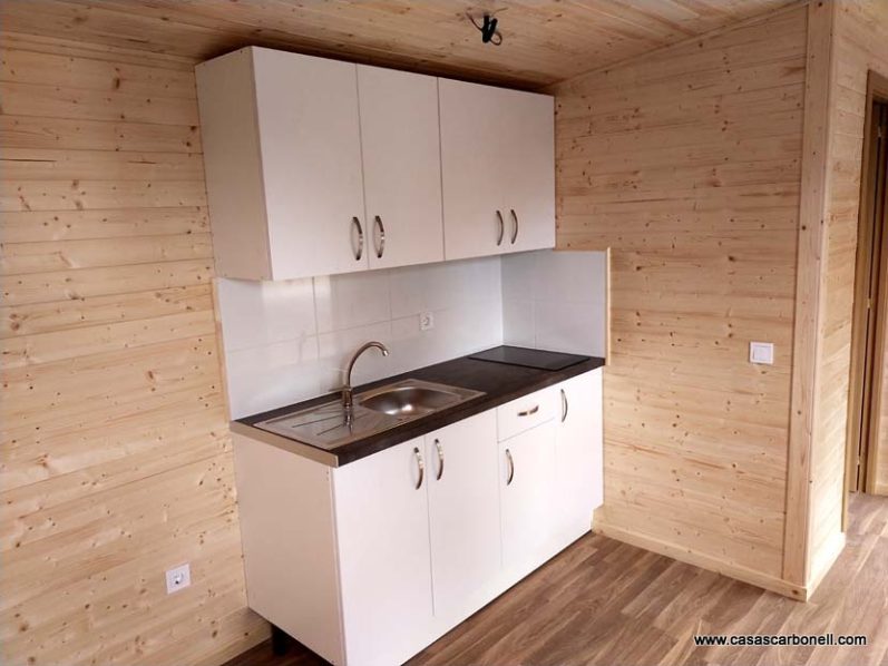Cocina moderna con armarios blancos y fregadero en un ambiente de madera clara.