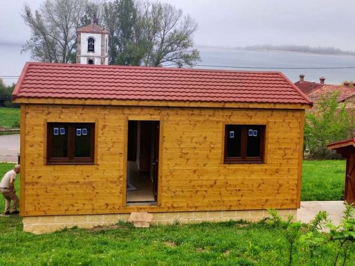 Casa prefabricada de madera con techo de tejas, ubicada en un entorno natural junto a un lago.