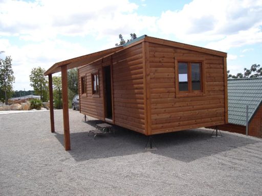 Casa de madera elevada sobre patas, con porche y ventanas, rodeada de grava.