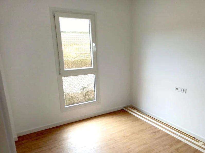 Habitación vacía con suelo de madera y ventana con luz natural.