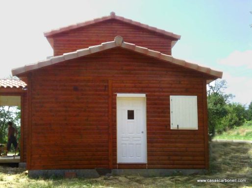 Casa prefabricada de madera con tejado a dos aguas y puerta blanca en un entorno natural.