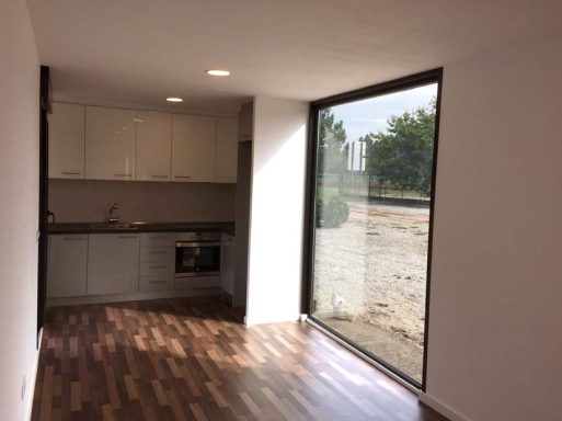 Interior de una cocina moderna con ventana grande y suelo de madera.