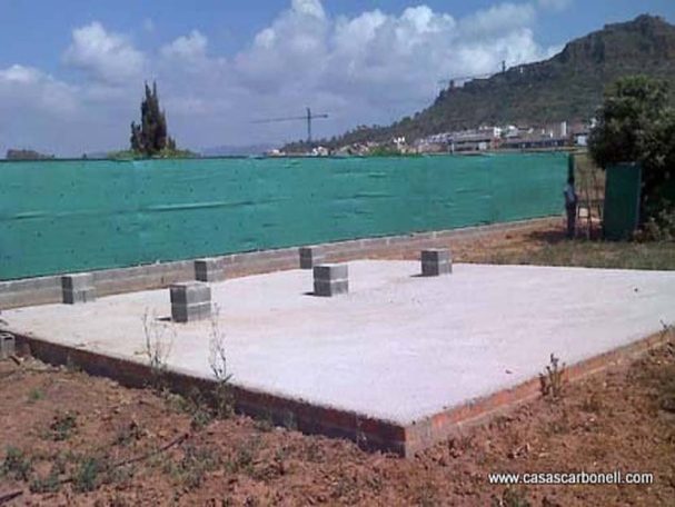 Base conformada sobre una losa de hormigón con pilares Base de hormigón con pilares en un terreno al aire libre, rodeada de vegetación.