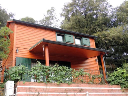 casa prefabricada de madera de color naranja con balcón, rodeada de vegetación.