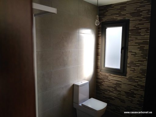 Baño moderno con ducha, inodoro y ventana iluminada. Paredes de azulejos oscuros.