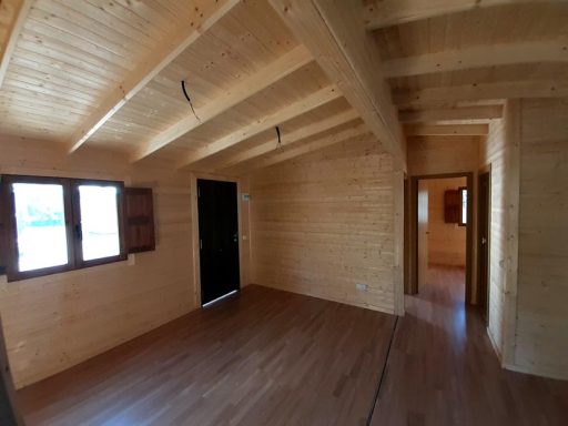 Interior de una cabaña de madera con ventanas, techo alto y suelos de madera.