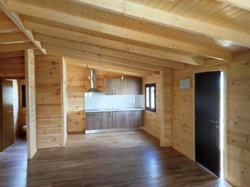 Interior de una casa de madera con techos altos y cocina abierta. Suelo de madera.