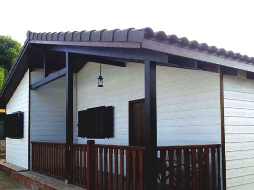 Casa prefabricada de campo con fachada blanca, techada a dos aguas y porche de madera.