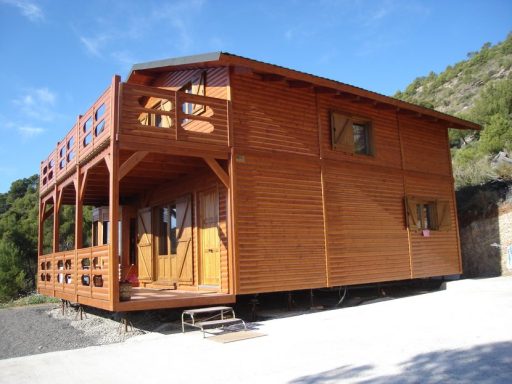 Casa prefabricada de madera con balcones, ubicada en un entorno natural montañoso.