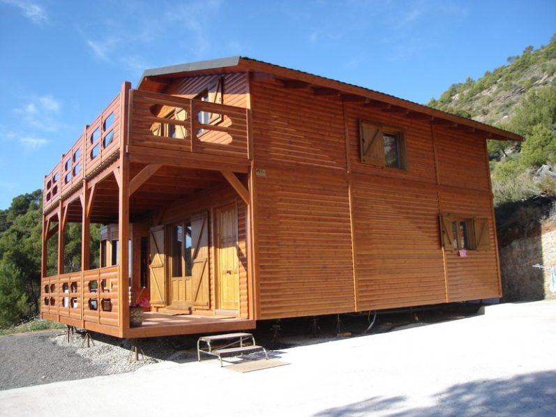 Casa prefabricada de madera con balcones, ubicada en un entorno natural montañoso.