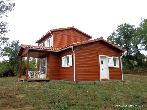 Casa prefabricada de madera de dos plantas, con techo a dos aguas y un porche frontal.