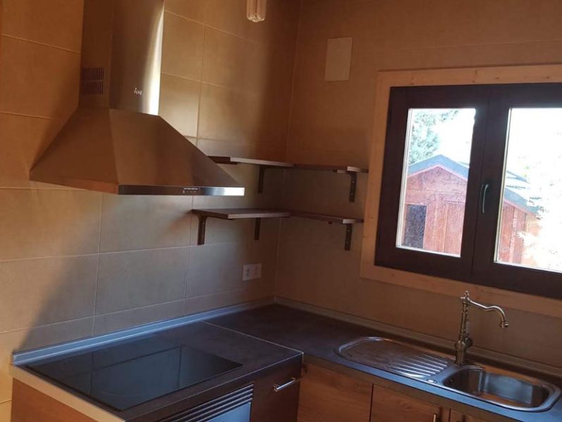 Cocina moderna con encimera, fregadero, y estantes abiertos bajo una ventana.