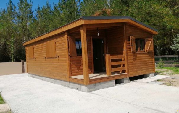 Casa prefabricada de madera con porche, ubicada en un entorno natural.