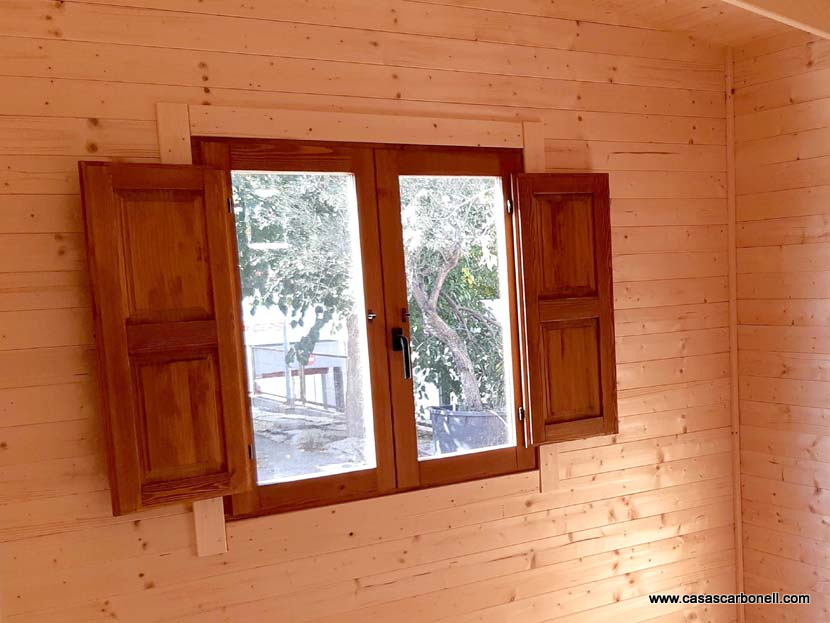 Ventana de madera con persianas abiertas, vista hacia un exterior arbolado.