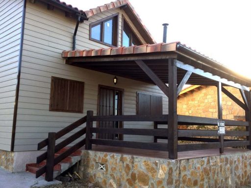 Casa prefabricada de dos plantas con porche, suelo de piedra y ventanas amplias.