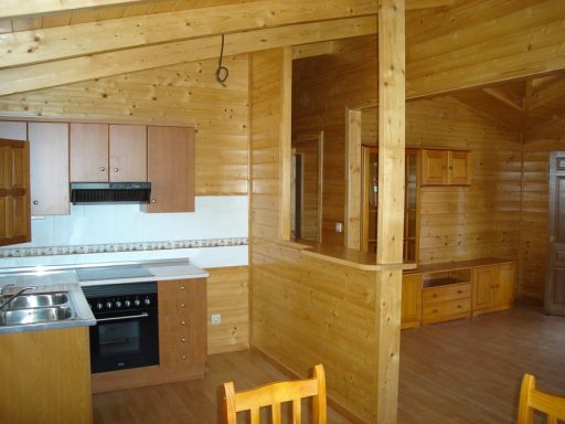 Cocina de madera con muebles sencillos y electrodomésticos, ambiente acogedor.